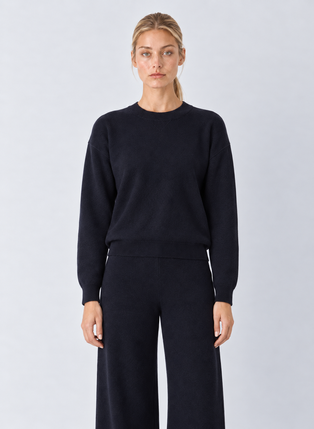 A woman modeling a dark navy crewneck sweater and matching wide-leg trousers against a light gray studio background.