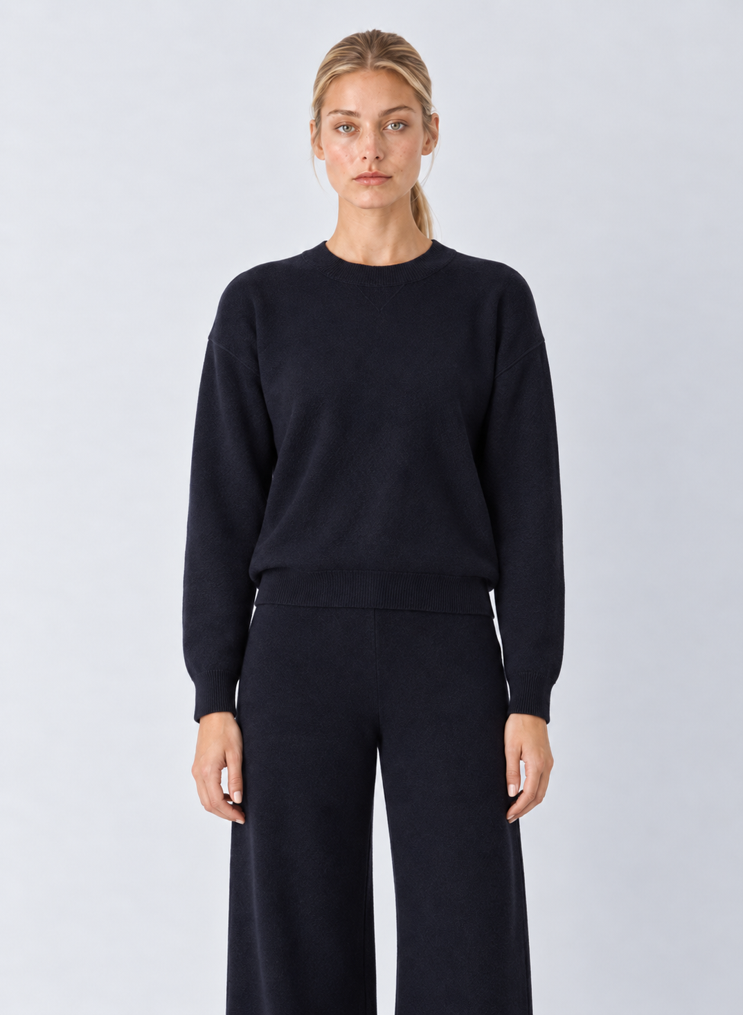 A woman modeling a dark navy crewneck sweater and matching wide-leg trousers against a light gray studio background.